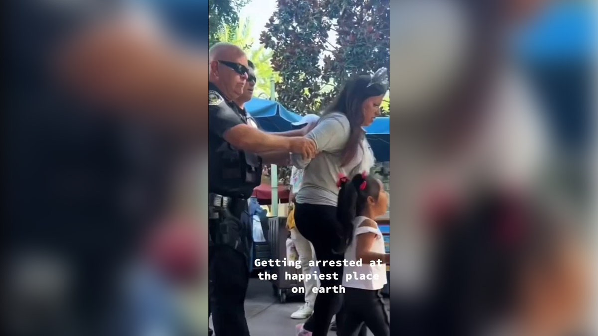 A woman is escorted by police out of Disneyland