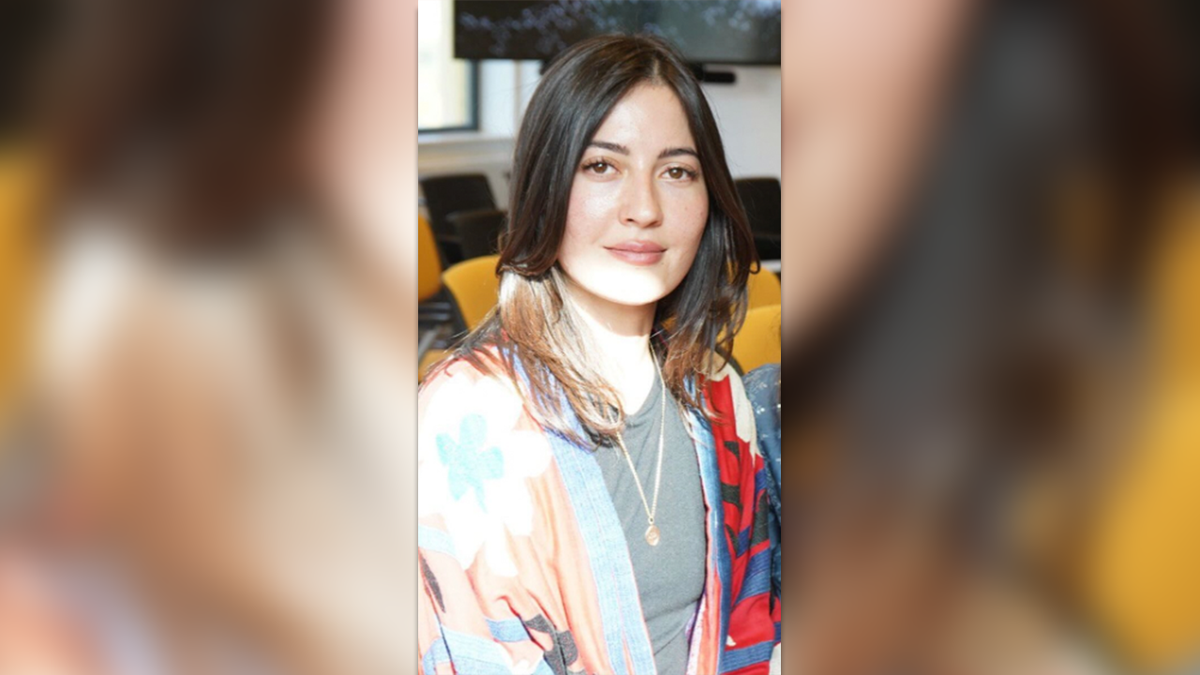 Sabina Rosas seated in a classroom with her hair down, sweating a colorful sweater over a T-shirt