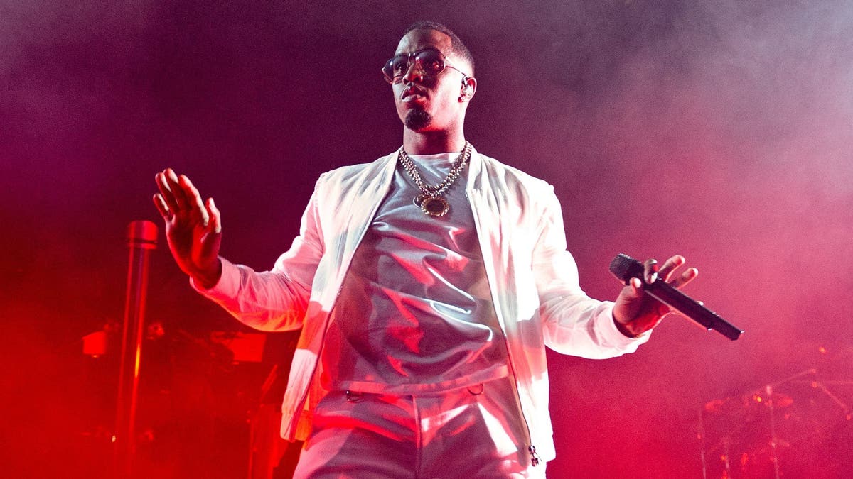 Diddy dances during a performance, wearing all white under red stage lights