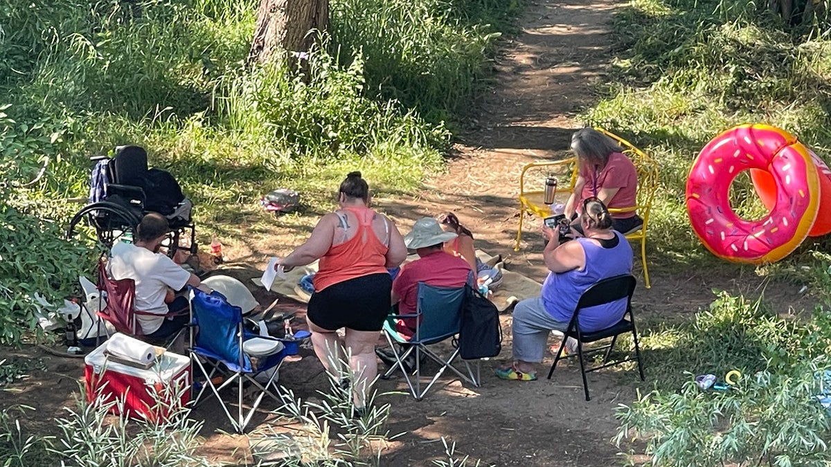 People sit in folding chairs on the beach next to Bear Creek