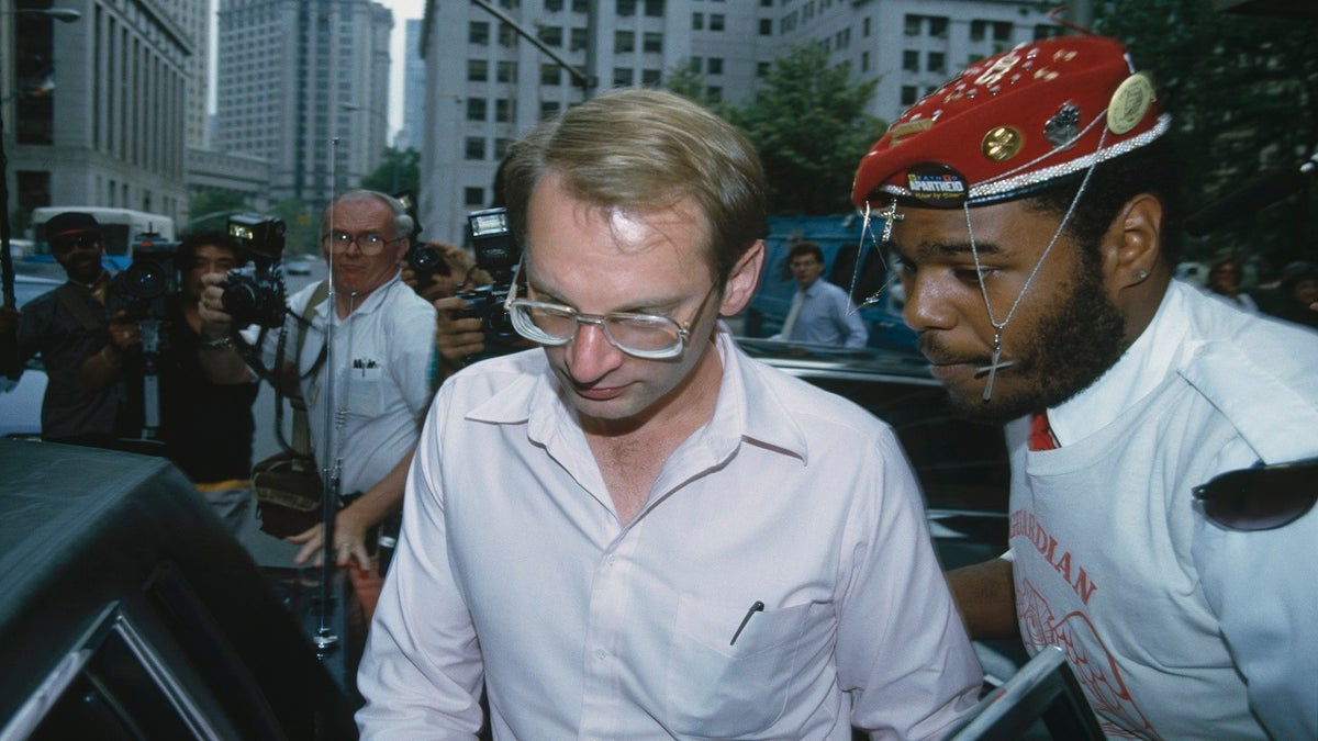 Bernhard Goetz leaves court wearing a white button-down shirt and glasses, surrounded by many people