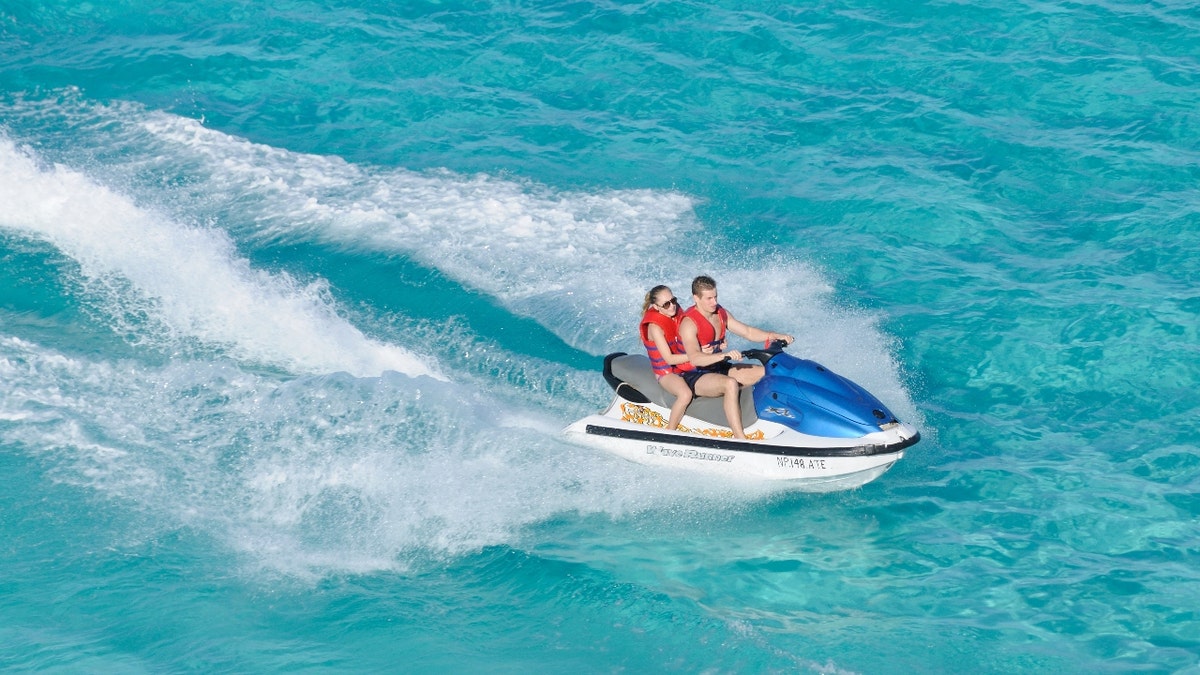 A man and woman ride on a jet ski in blue water.