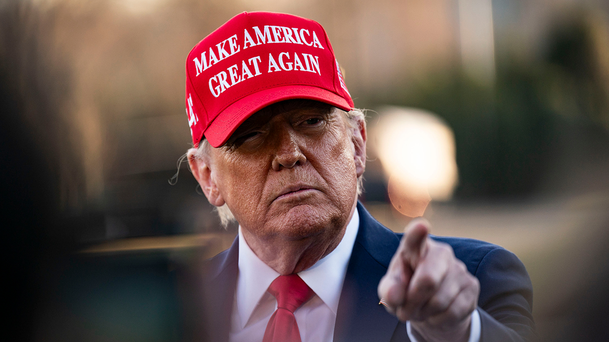 Trump wearing a red Make America Great Again hat and pointing