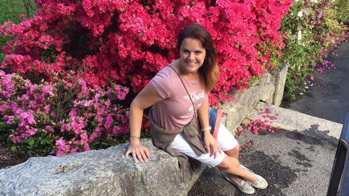 Angela Craig sits on rock wall with pink flower bush in background