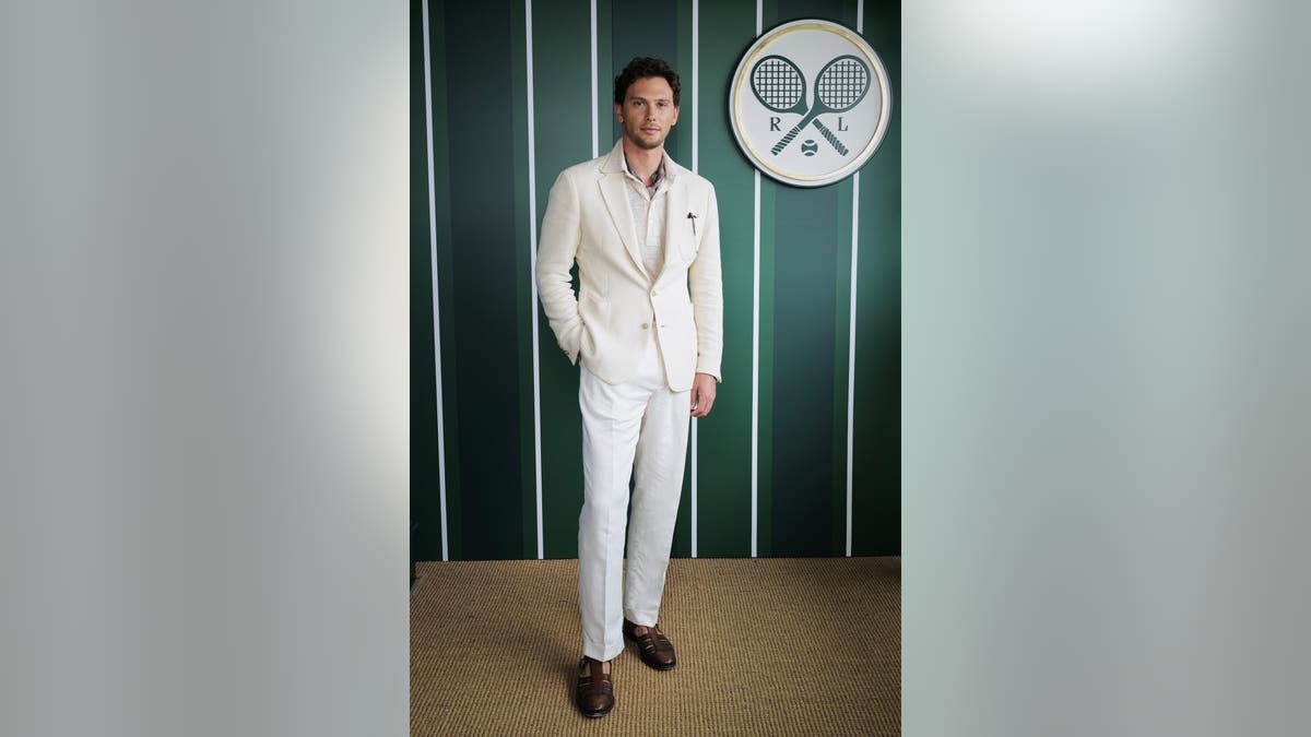 Kooper Koch in a light-colored suit in front of a green wall marked with Tennis Rackets