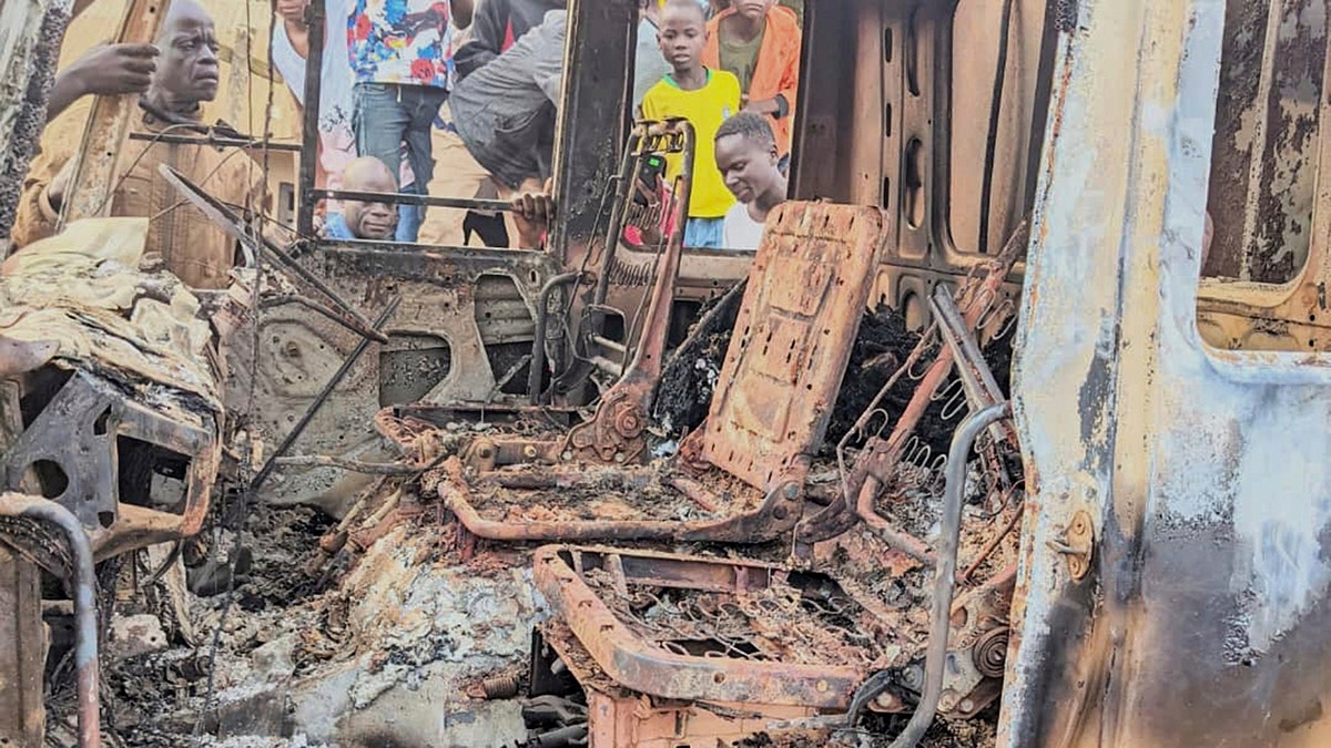 People gather around the charred remains of a burned vehicle following a deadly attack in Komanda, Ituri province of eastern DR Congo, where 49 worshipers were killed at a church service by jihadists.