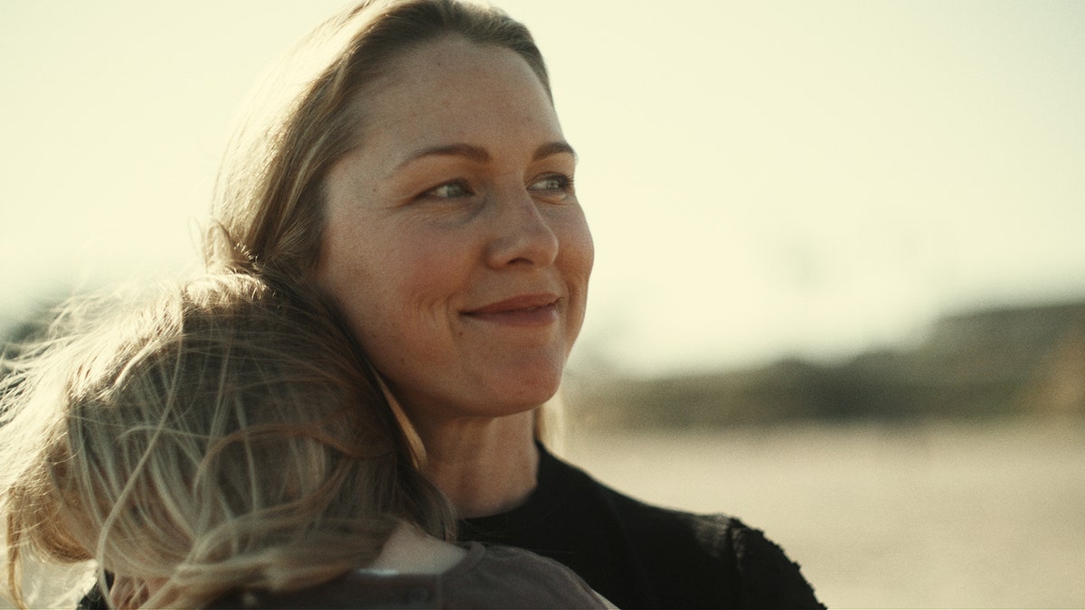 Denise Huskins holding a child at the beach and smiling.
