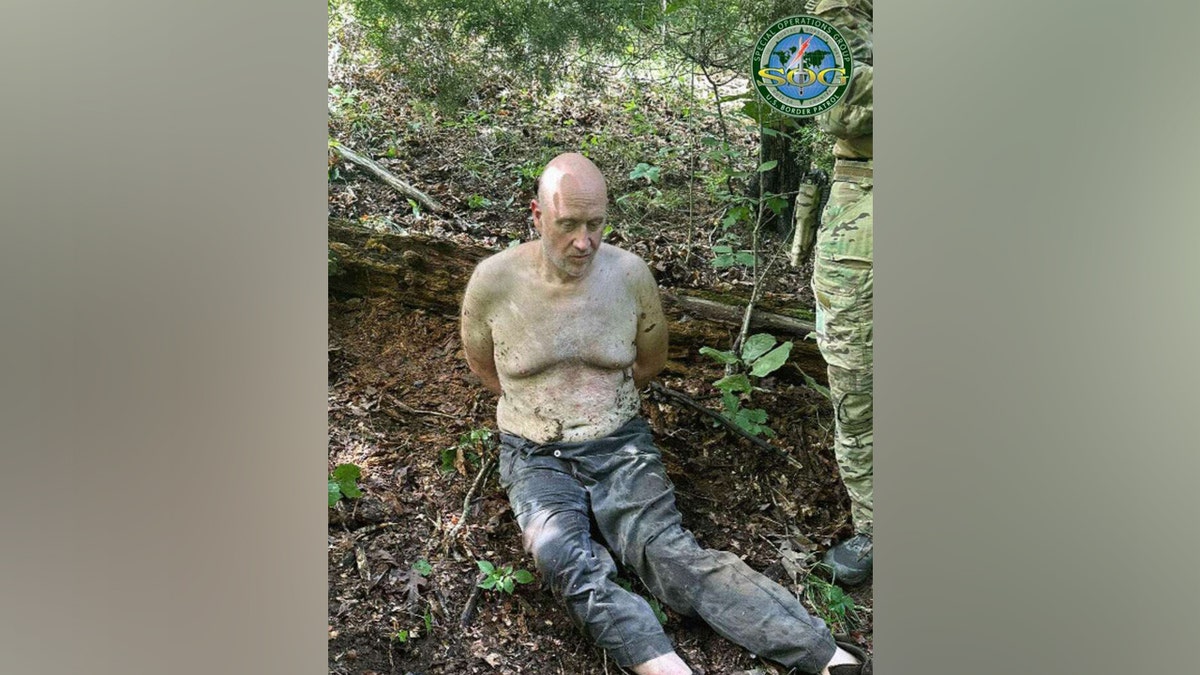 Grant Hardin sitting shirtless in the woods after his capture