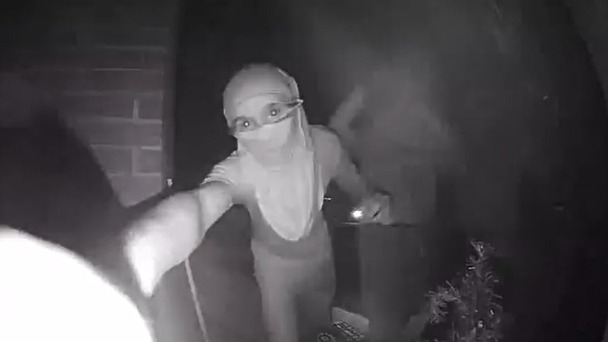 A person wearing a shirt around their face presses a security camera doorbell