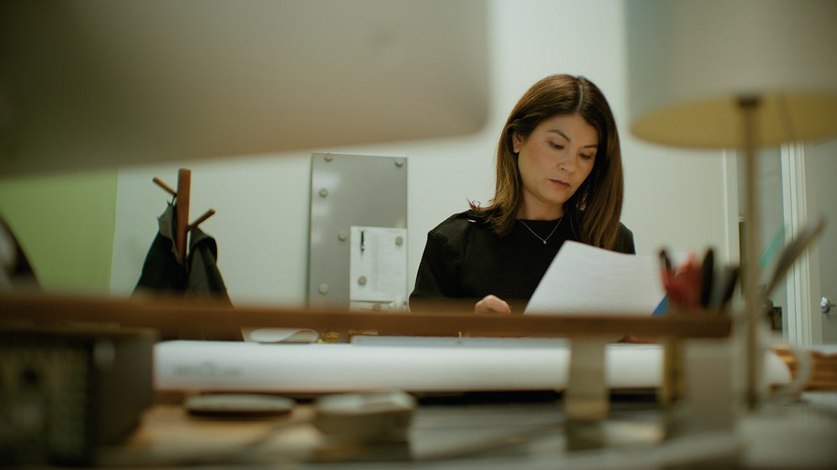 Maria Awes in black looking at paperwork from a desk.