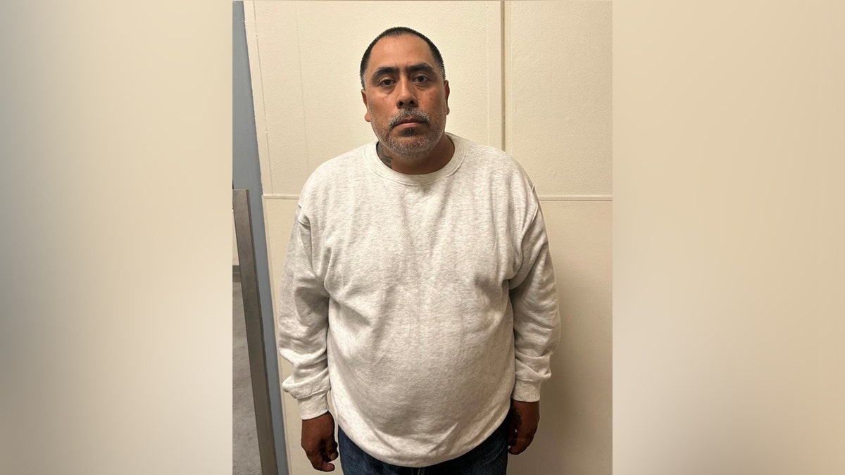 An illegal alien farmworker poses for booking photo in long-sleeved white shirt