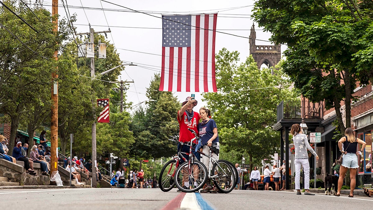 A couple takes a photo of the center traffic line painted in red, white and blue before a Fourth of July parade begins Saturday, July 4, 2020, in Bristol, R.I.