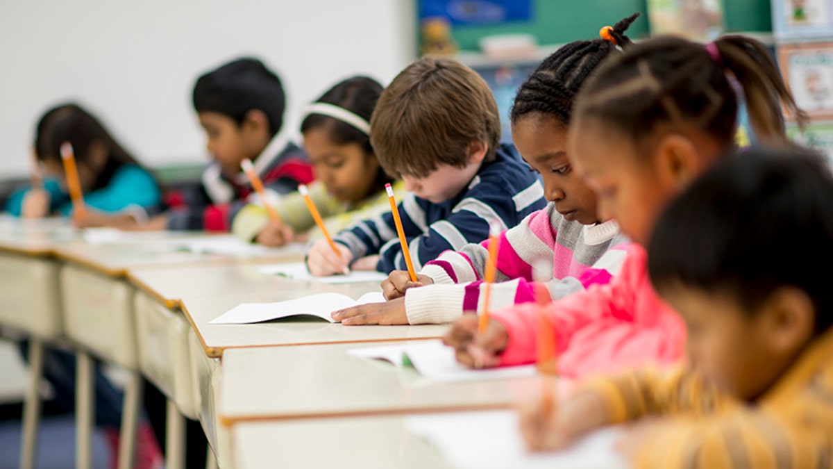 children at desks writing in classroom, stock photo