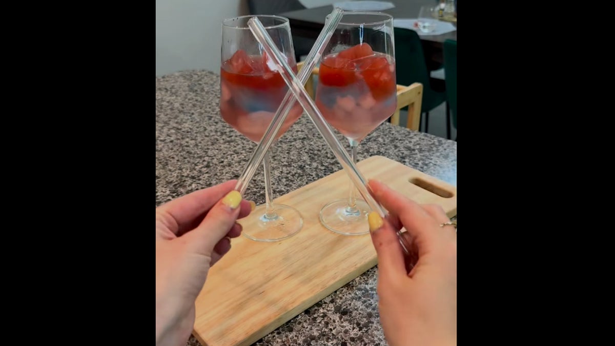 Screenshot of TikTok video showing two red, white and blue drinks in wine glasses, with woman's hands holding straws in front of them getting ready to serve them.