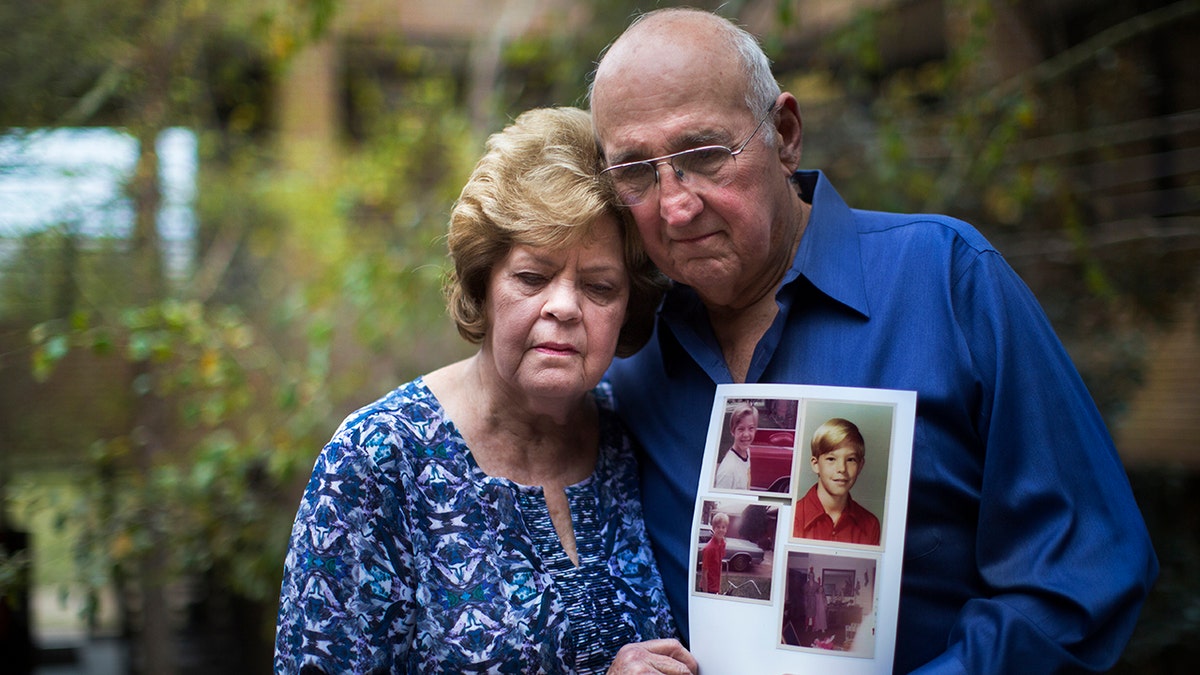 A man and a woman wearing blue looking heartbroken as they hold photos of a murder victim.