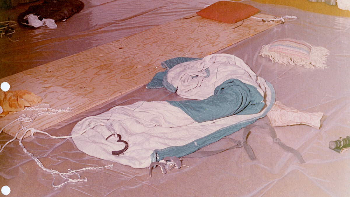 Dean Corll's torture board on a bed next to clothing and handcuffs.