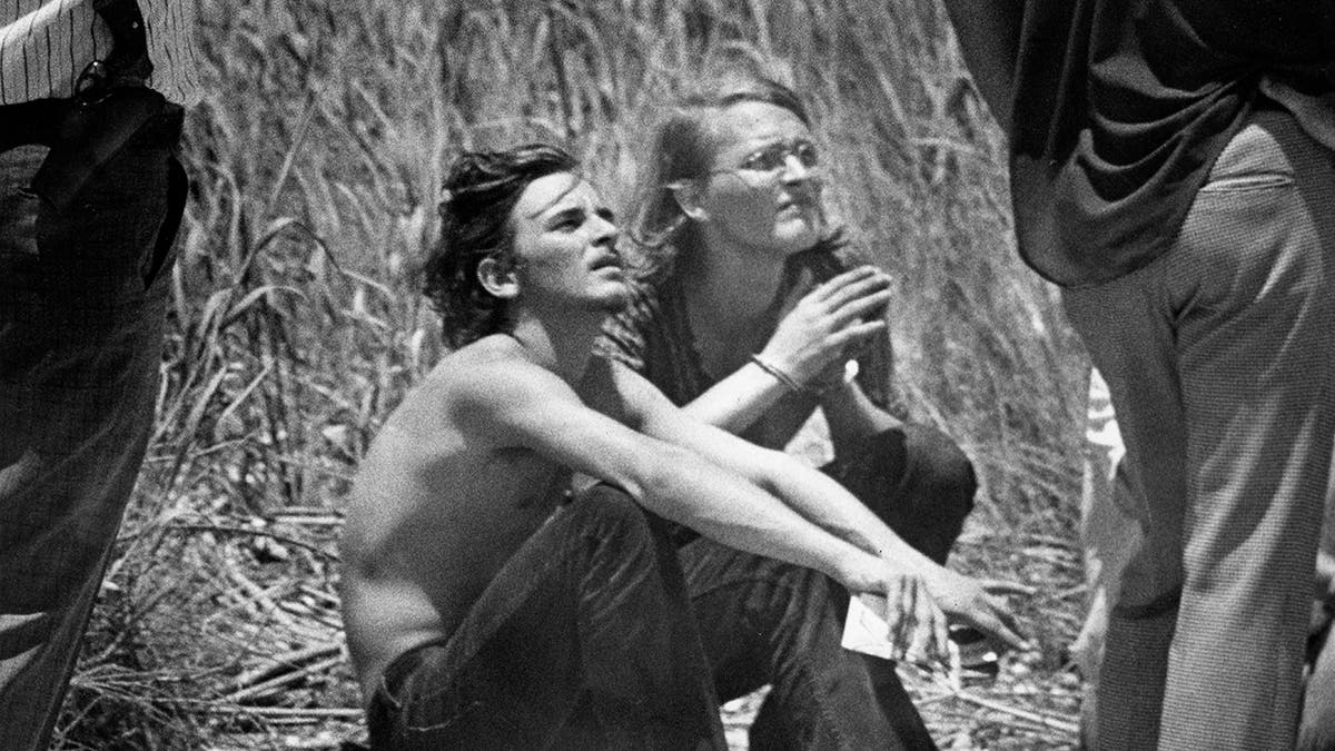 Elmer Wayne Henley and David Brooks sitting down in a field and looking up.