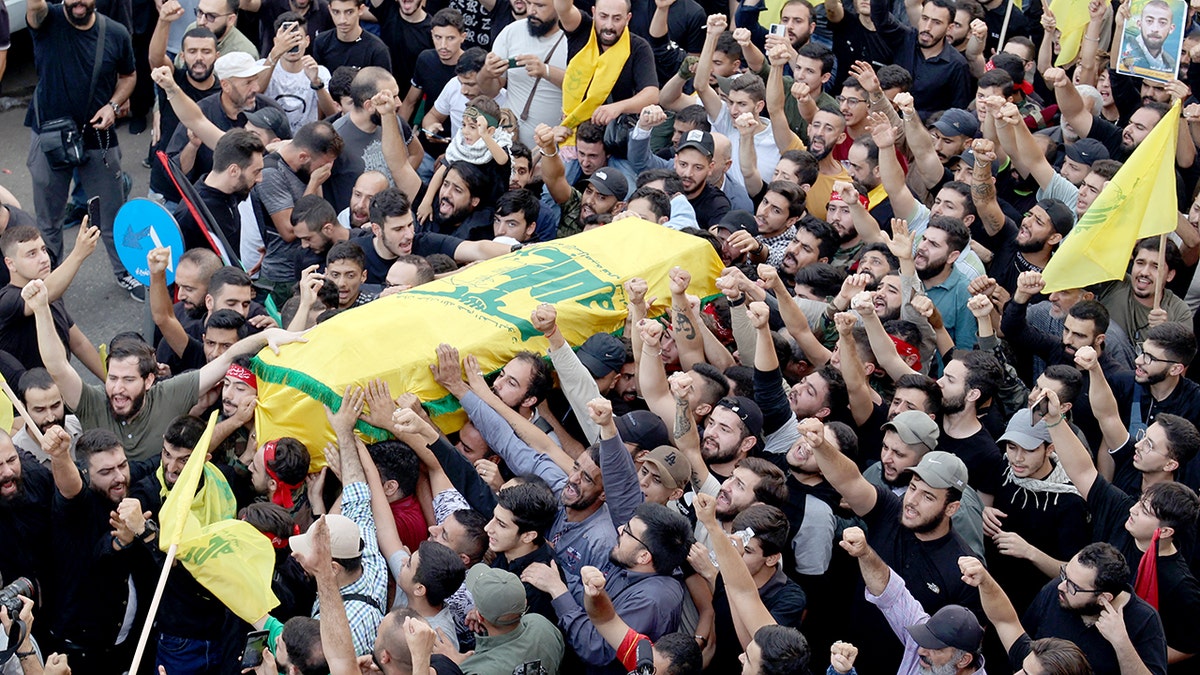 Mourners crowd around coffin with Hezbollah flag