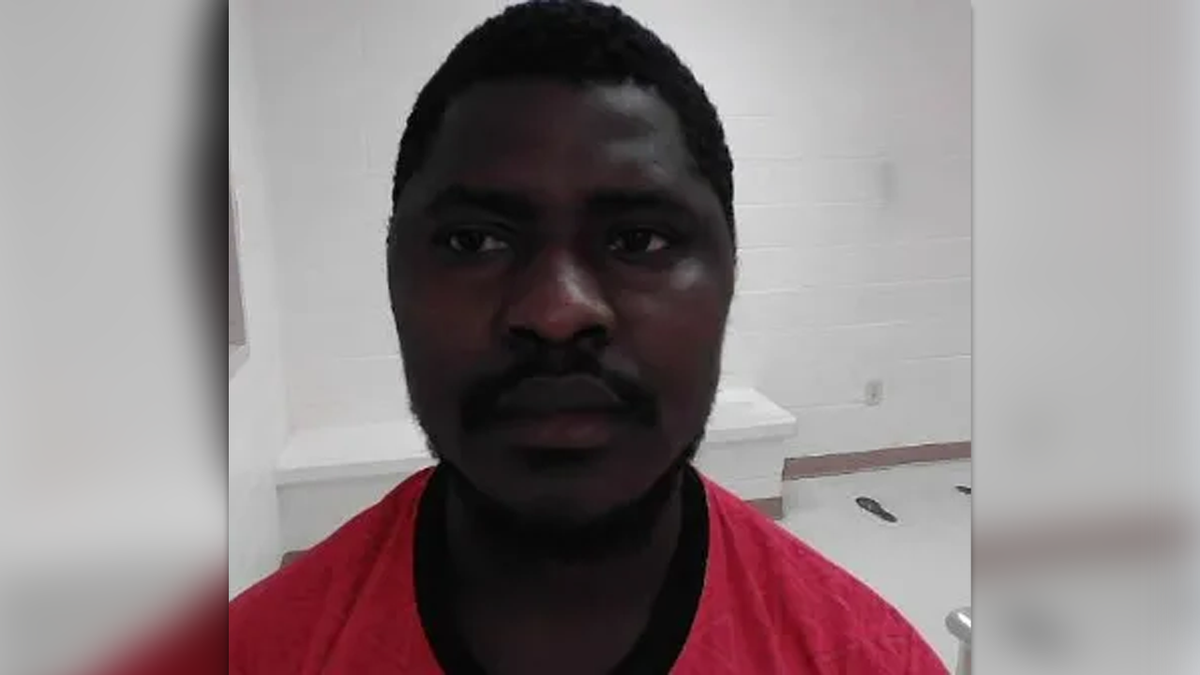 Lionel Francisco in a white jail room wearing a red t-shirt in his booking photo