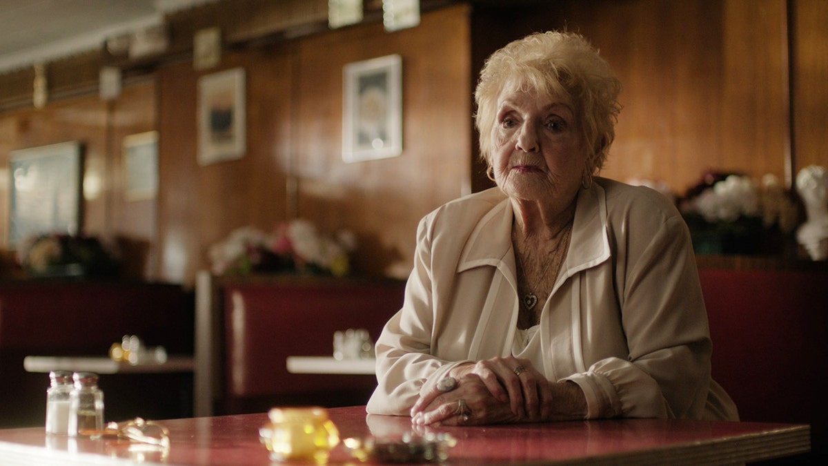 Wendy Savino wearing a white blouse sitting in front of a wooden desk.