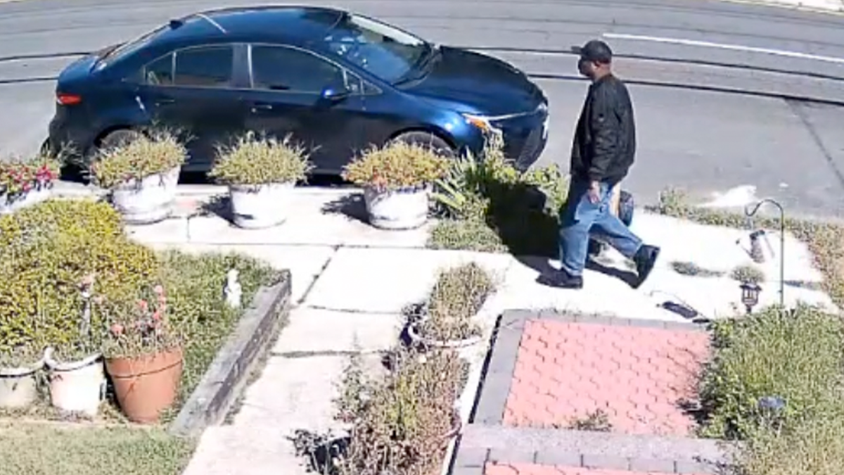 suspect walking in a black hat, black jacket, black sneakers and bluejeans, seen carrying what appear to be two bags in his right hand