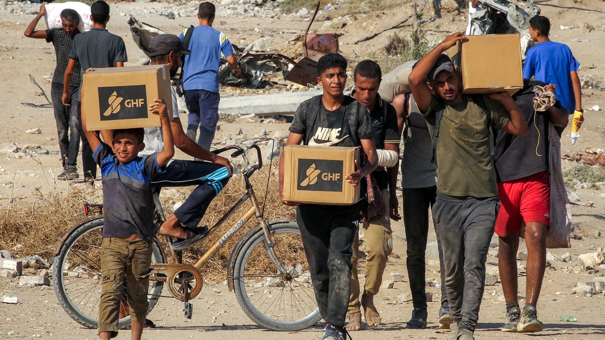 Gazans walk with boxes of humanitarian aid they received at a distribution center run by the U.S. and Israeli-backed Gaza Humanitarian Foundation (GHF).