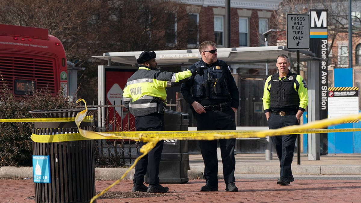 Police officers stand outside with caution tape around them