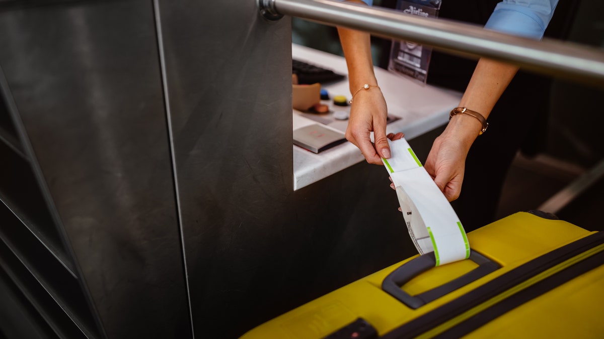 An airport attendant attaches a label on a suitcase at an airline check-in desk.