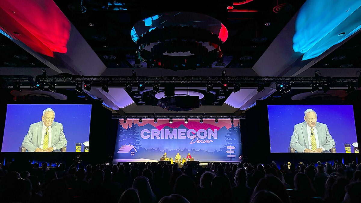 John Ramsey, his lawyer and journalist Paula Woodward sit on stage at a conference