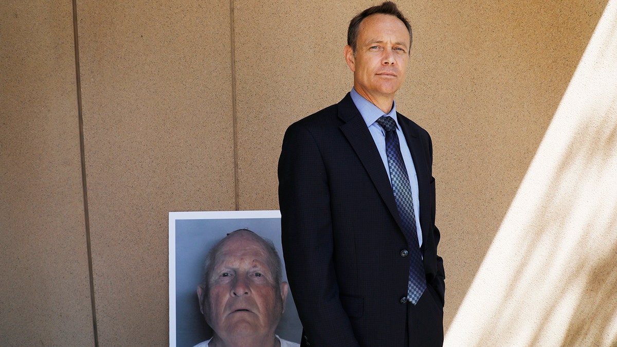 Paul Holes in a suit standing next to the mugshot of the Golden State Killer.