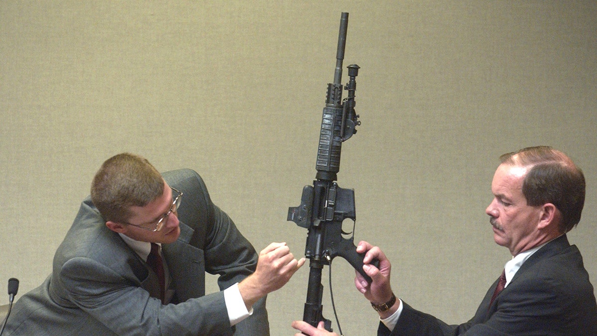 Two investigators holding a gun in court.