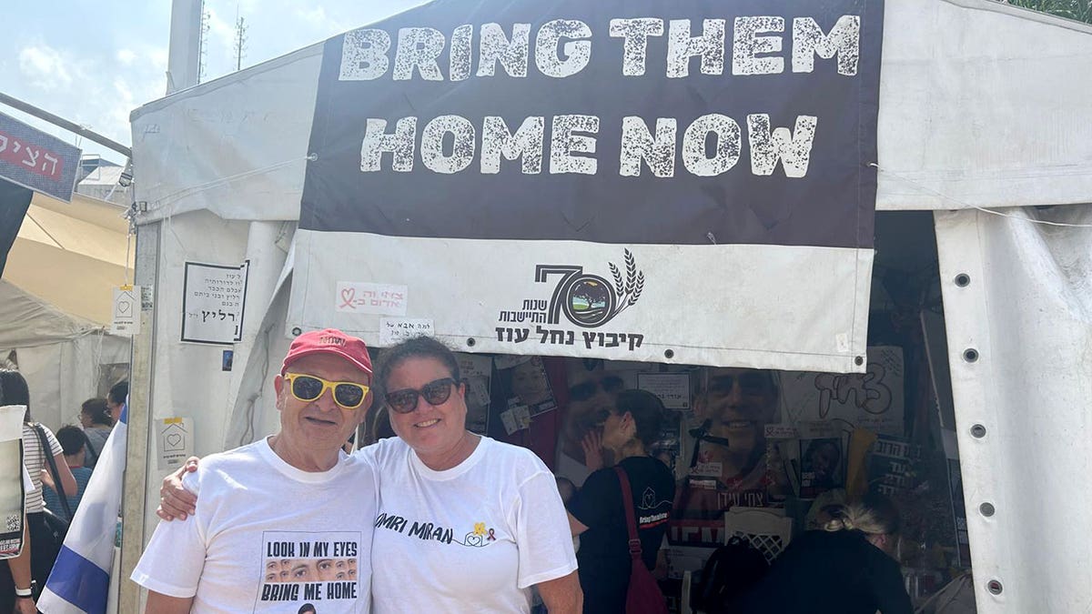 Man and woman stand smiling outside tent with