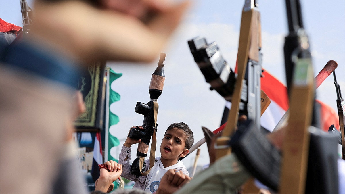 Boy holding toy gun surrounded by protesters holding guns.