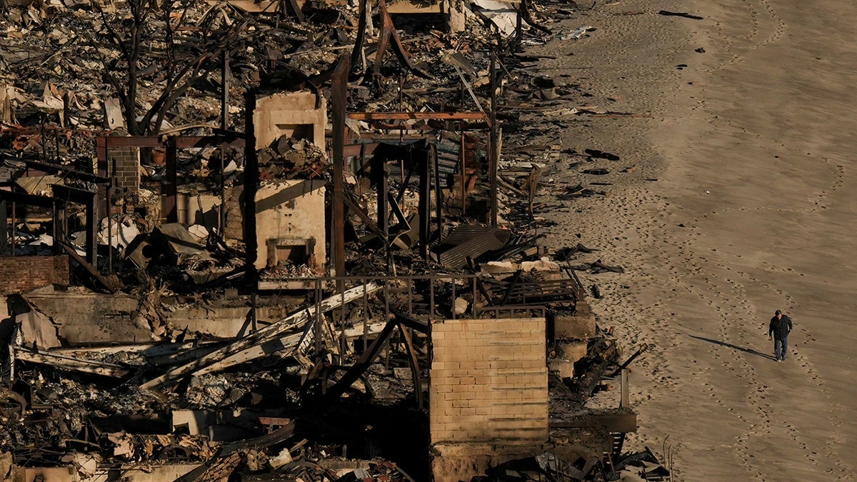 Person walks by homes destroyed by Palisades Fire in California