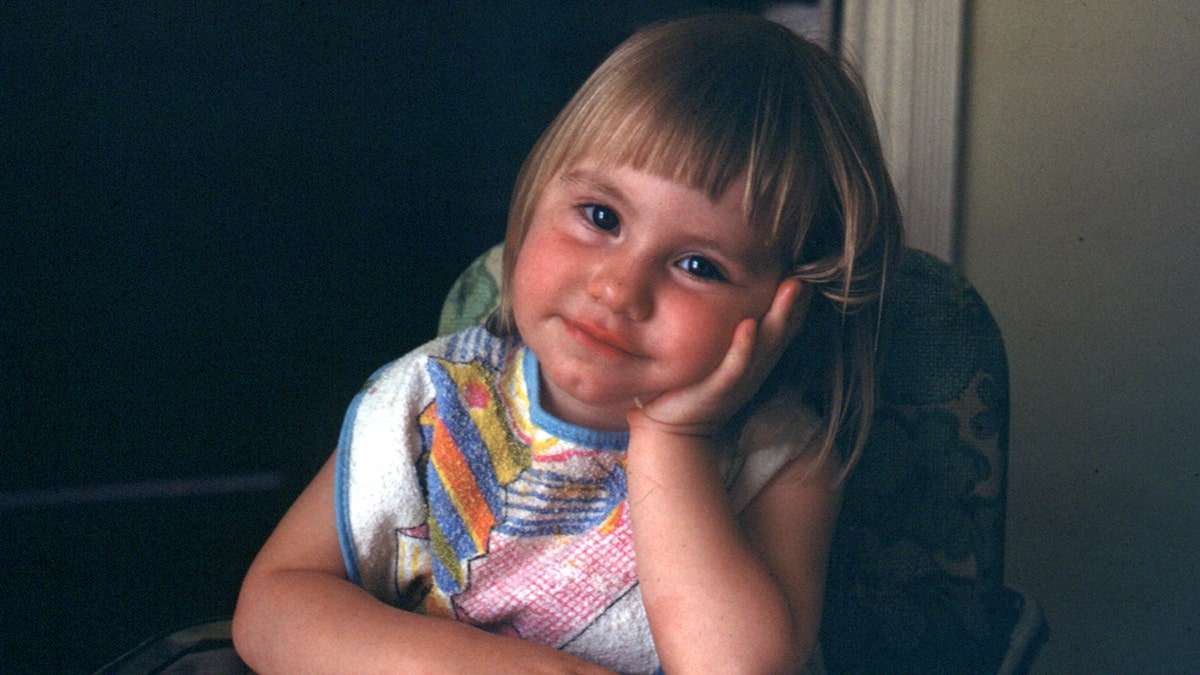 Rebecca Lafferty as a toddler looking at her father for a photo as she sits on a high chair.
