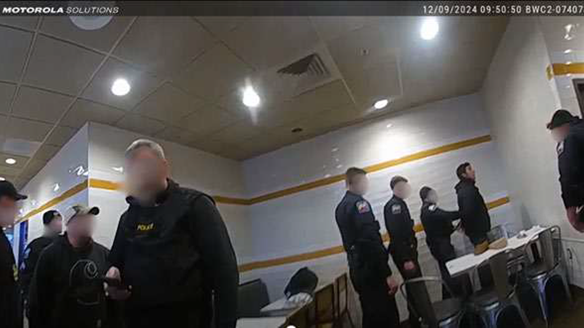 A man identified as Luigi Mangione is placed in handcuffs as a large number of police officers fill up the frame