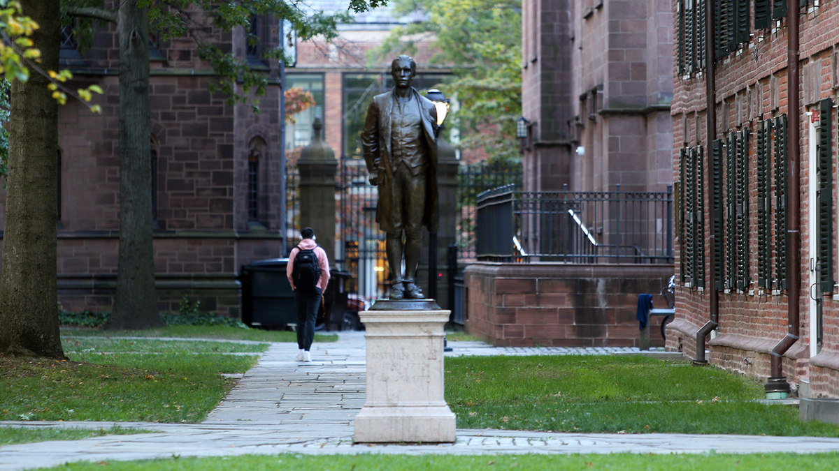 A student walks behind a bronze statue in Yale's Old Campus Courtyard