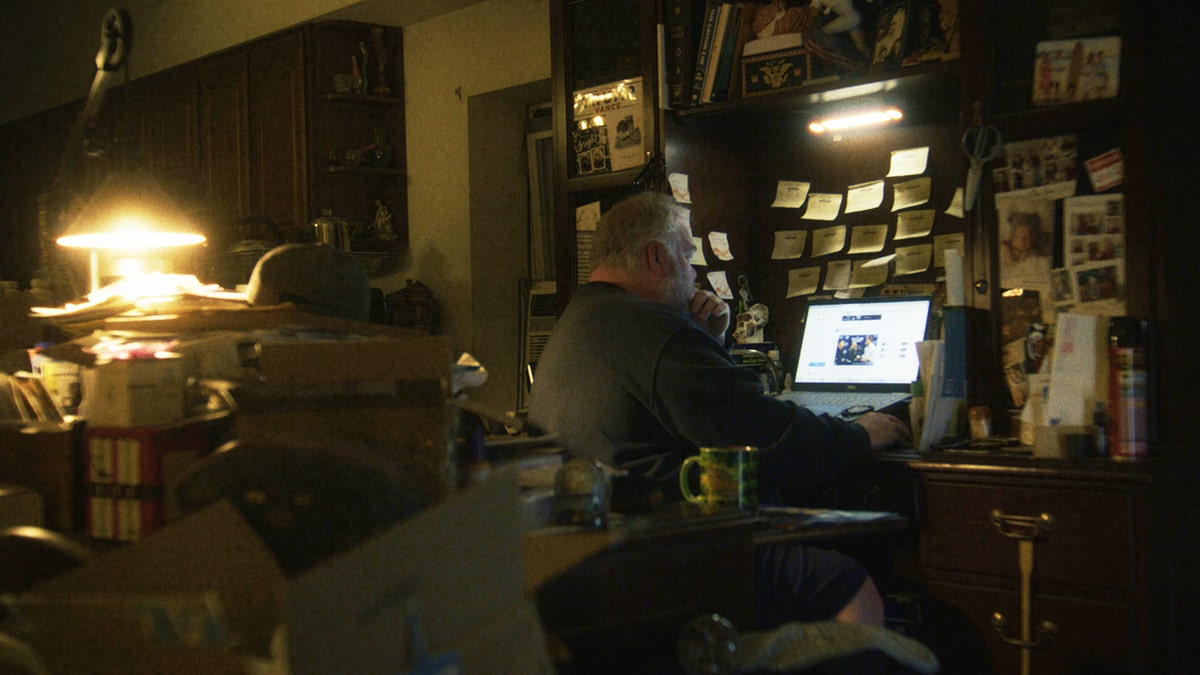Michael Carroll looks at Facebook in his laptop at his messy desk in his home.