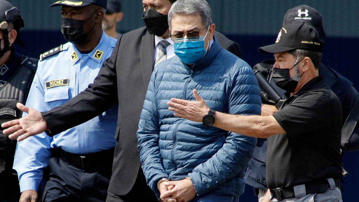 Juan Orlando Hernandez, in handcuffs, is directed toward aircraft