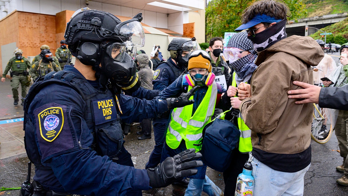 Law enforcement officers and demonstrators confront each other outside a secured federal building during a protest.