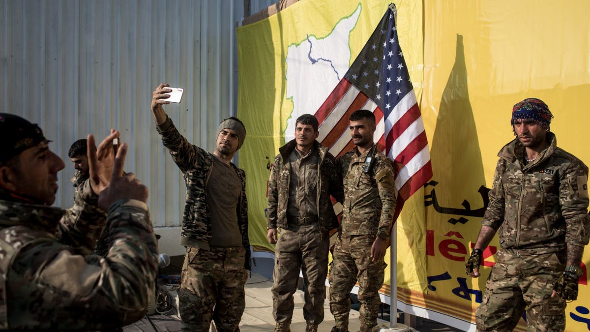 Syrian Democratic Forces (SDF) fighters pose for a photo with the American flag on stage after a SDF victory ceremony announcing the defeat of ISIL in Baghouz was held at Omer Oil Field on March 23, 2019 in Baghouz, Syria. 