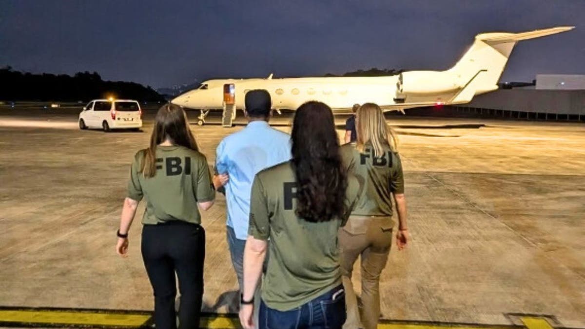 FBI agents escorting a man across an airport tarmac toward a private jet during extradition.