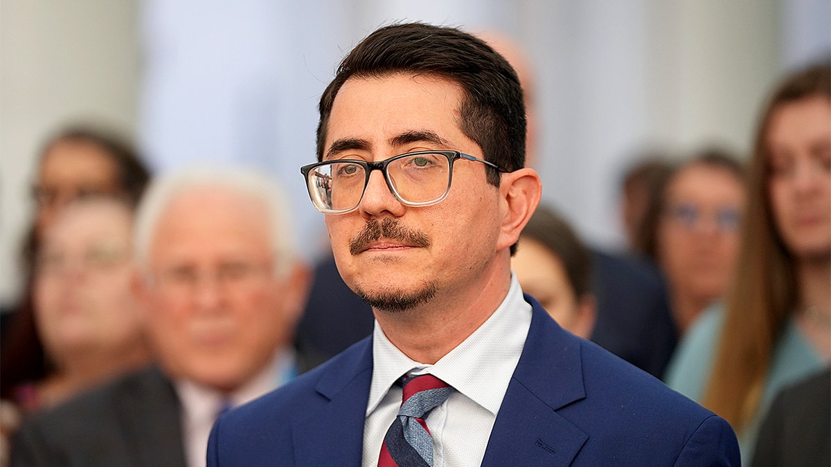 Jose Garza speaking at a wooden lectern during a news conference at the Blackwell-Thurman Criminal Justice Center.
